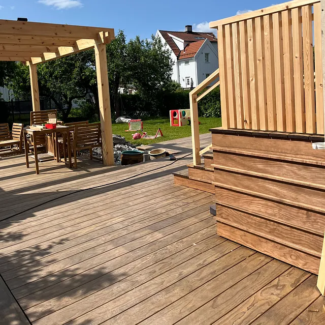 Utemøbler i tre med vase med røde roser på bordet.